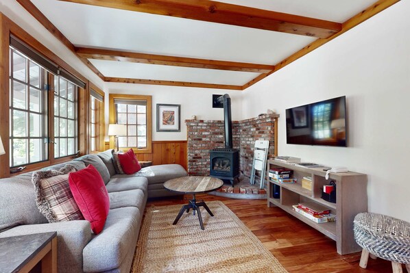 A cozy living room with a sofa, a round coffee table, a fireplace, and a TV mounted on the wall. - Cute cabin with spacious porch, walk to beach & dining, central to ski resorts (Carnelian Bay)