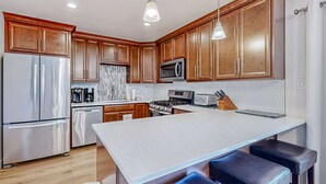 A modern kitchen with wooden cabinets, stainless steel appliances, a large island with bar stools, and pendant lighting. - Quiet mountain home with game room & fireplace - near scenic trails & ski slopes (Incline Village)