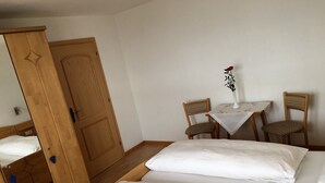 A room with two beds, a wooden wardrobe, a table with chairs, and a vase with a flower. - Apartment 'Nunnenmayr A' with Mountain View, Shared Garden and Wi-Fi (Tirolo)