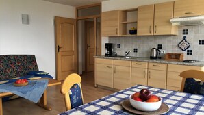 A compact kitchen with wooden cabinets, a tiled backsplash, a coffee maker, and a table with a checkered tablecloth. - Apartment 'Nunnenmayr A' with Mountain View, Shared Garden and Wi-Fi (Tirolo)
