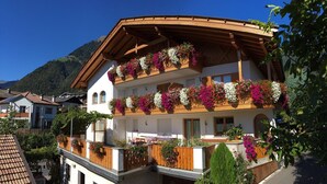 A multi-story building with balconies adorned with flower boxes, surrounded by greenery and a mountainous backdrop. - Apartment 'Nunnenmayr A' with Mountain View, Shared Garden and Wi-Fi (Tirolo)