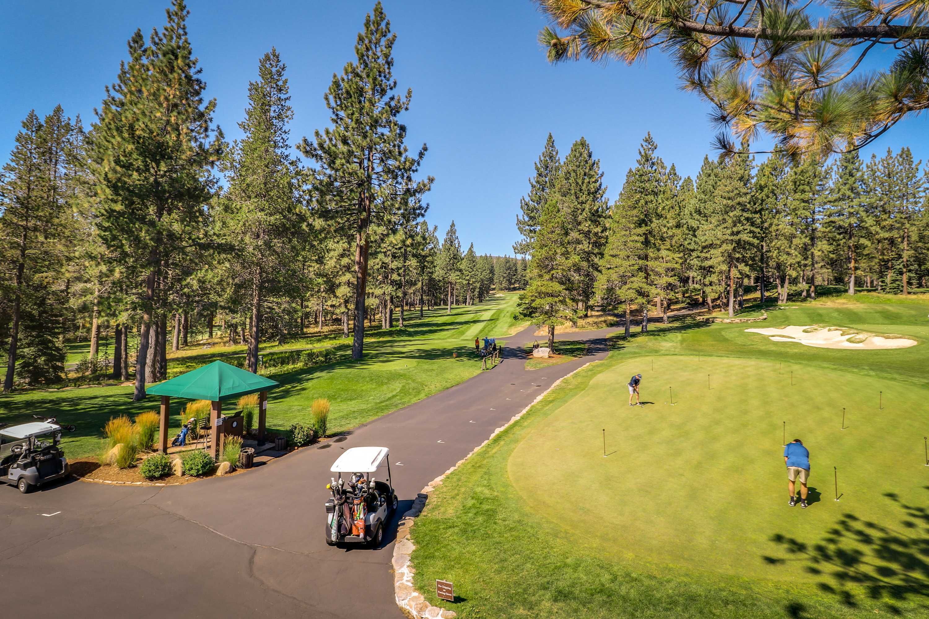 A golf course with a gazebo, a golf cart, and a clear sky.