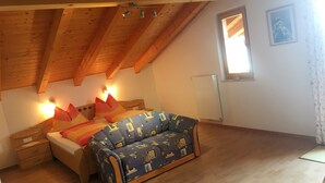 A bedroom with a sloped ceiling, a bed with patterned bedding, a sofa, a nightstand, and a window with a view. - Apartment 'Nunnenmayr B' with Mountain View, Shared Garden and Wi-Fi (Tirolo)