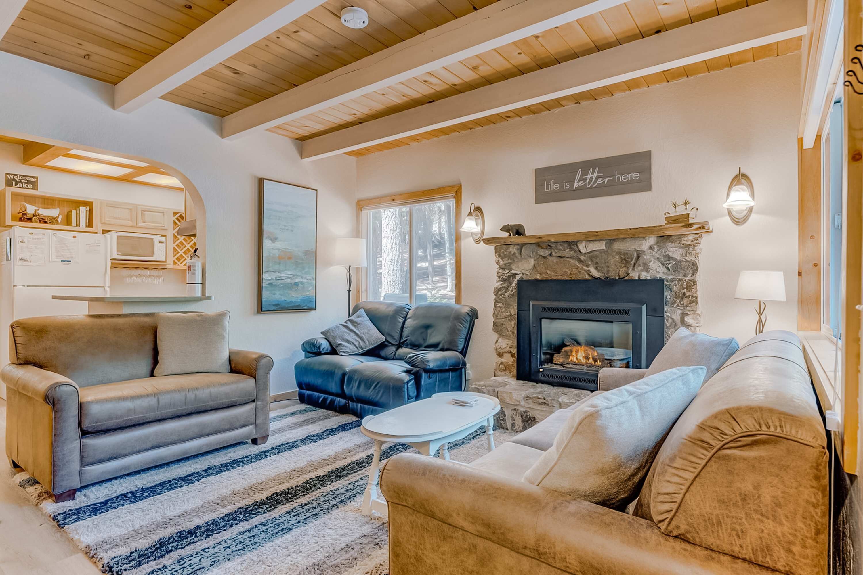 A cozy living room with a fireplace, leather sofas, a kitchen area, and a view of the outdoors.