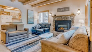 A cozy living room with a fireplace, leather sofas, a kitchen area, and a view of the outdoors. - close to beach & skiing with grill, fireplace, deck, & W&D (Tahoma)