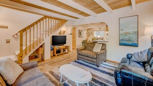 A spacious living area with a wooden staircase, a flat-screen TV, and a large painting on the wall. - close to beach & skiing with grill, fireplace, deck, & W&D (Tahoma)