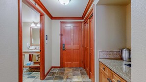 A hallway with a wooden door, a kitchen area with granite countertops, and a tiled floor. - Ski-in-ski-out studio in Everline Resort & Spa - pools, gym, tennis, ice rink (Olympic Valley)