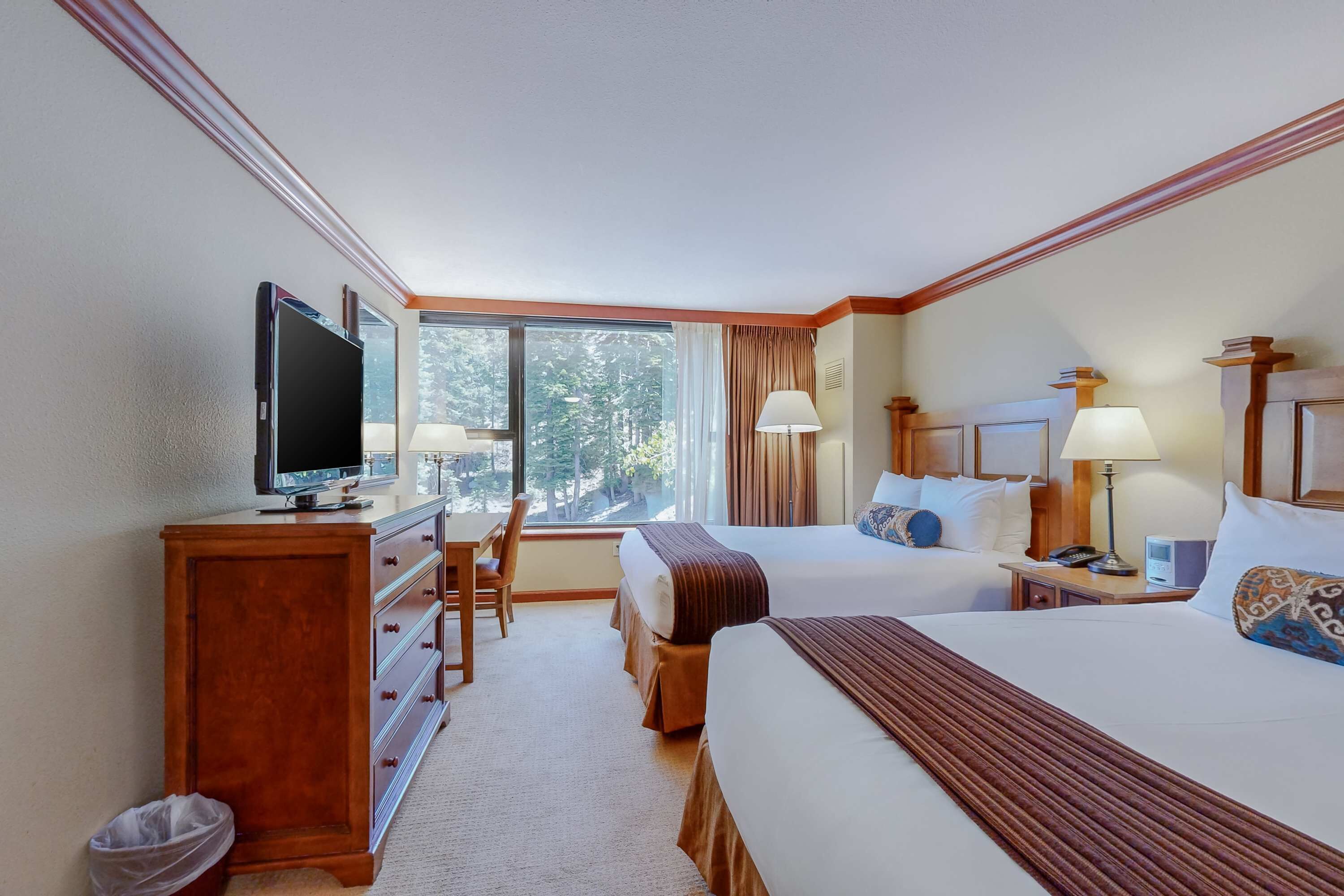 A hotel room with two beds, a desk, a television, and a window with curtains.
