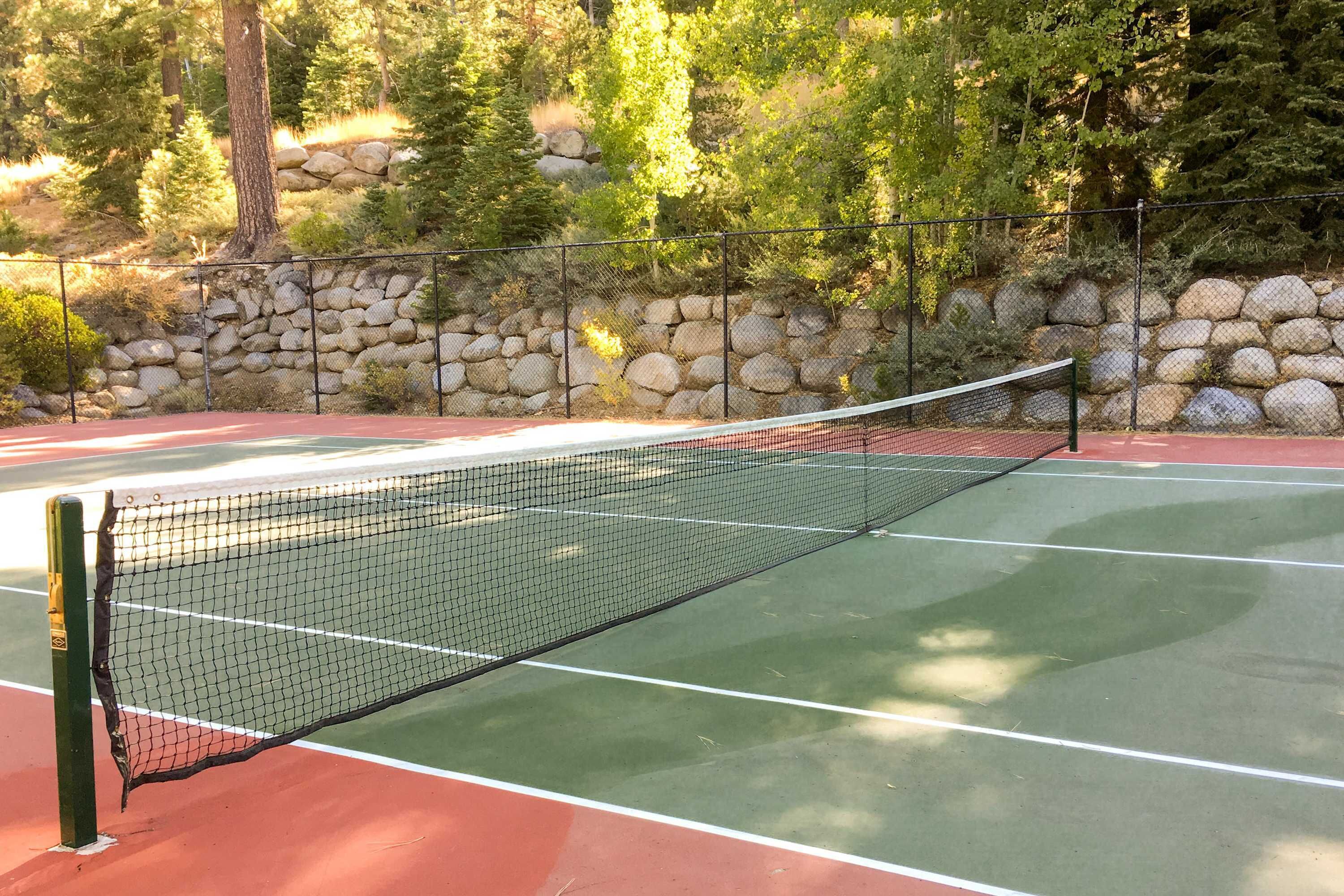 Ein Tennisplatz mit Netz, umgeben von einer Steinmauer und Bäumen.