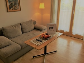A living room with a sofa, a table with apples and a book, a lamp, and a window with curtains.