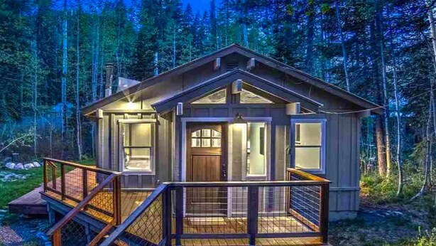 A cabin with a wooden deck, a front door, and a staircase leading up to it.