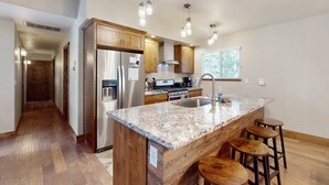 A kitchen with wooden cabinets, stainless steel appliances, a granite countertop, and bar stools.