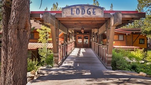 Ingresso di un lodge con una tettoia che conduce all'edificio, immerso tra alberi e un cielo sereno.