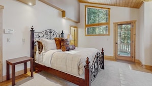 A bedroom with a wooden bed, a nightstand, a ceiling fan, and a large window with a view of trees. - Stunning Large Custom Family Home with Fireplace, Hot tub, Yard, & Views! (South Lake Tahoe)