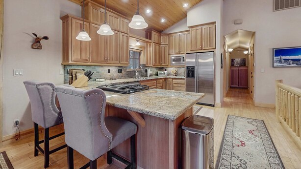 A kitchen with wooden cabinets, a granite island, pendant lights, and a stainless steel refrigerator. - Stunning Large Custom Family Home with Fireplace, Hot tub, Yard, & Views! (South Lake Tahoe)