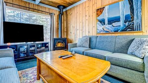 A cozy living room with a fireplace, a large TV, and a sofa. - Dog Friendly Cabin with Hot Tub & Fireplace near Camp Richardson (South Lake Tahoe)