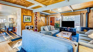 A cozy living room with a fireplace, a television, and a dining area with chairs and a table. - Dog Friendly Cabin with Hot Tub & Fireplace near Camp Richardson (South Lake Tahoe)