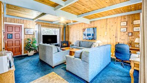 A cozy living room with a fireplace, a sofa, a television, and a dining area. - Dog Friendly Cabin with Hot Tub & Fireplace near Camp Richardson (South Lake Tahoe)