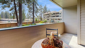 A balcony with a wicker basket of pinecones, a chair, and a view of a building and trees.