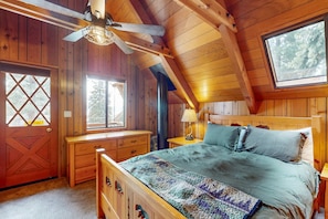 Ein Holzhütten-Interieur mit einem Bett, einem Schreibtisch, einem Fenster und einem Deckenventilator.