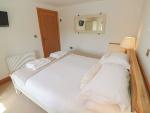 A neatly made bed with white linens, a wooden headboard, a bedside lamp, a mirror, and a radiator. - Ash Barn (Falmouth)
