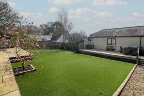 A well-maintained lawn with a stone border, a wooden deck, and a building with a balcony. - Ash Barn (Falmouth)