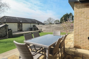 A patio with a table and chairs, a brick wall, and a grassy lawn. - Ash Barn (Falmouth)