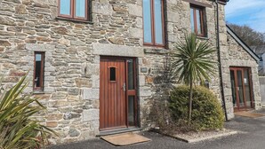 Ein Steinhaus mit einer Holztür, Fenstern und einem kleinen Garten mit Pflanzen.