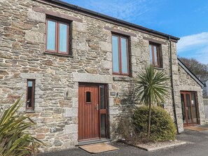 A stone building with a wooden door, windows, and a small garden area with plants. - Ash Barn (Falmouth)