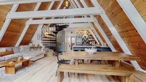 A loft-style interior with a wooden floor, a sofa, a dining table, and a kitchen area. - Beautiful A-frame home with deck, streaming, and dog friendly - near skiing (South Lake Tahoe)