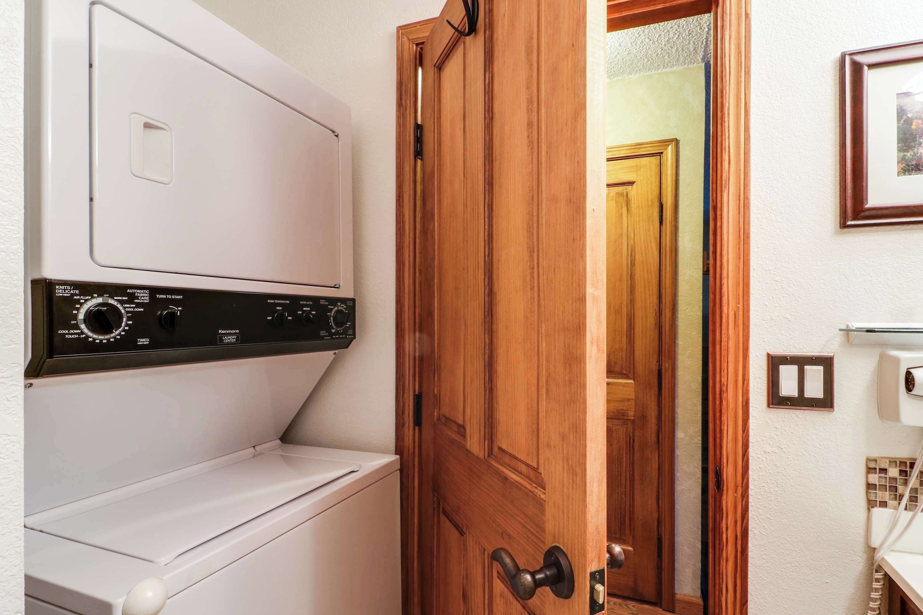 Un espace buanderie comprenant un lave-linge et un sèche-linge, une porte en bois et un tableau encadré accroché au mur.