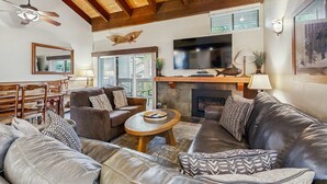 Una sala de estar acogedora con chimenea, sofás de cuero, techo de madera y televisor montado sobre la chimenea.