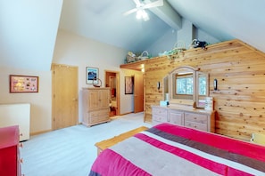 A bedroom with a sloped ceiling, wooden walls, a bed with a red and gray bedspread, a dresser, a mirror, and a ceiling fan. - Charming Tahoe Donner home with 2 fireplaces & washer&dryer (Truckee)