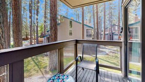A covered deck with a mesh railing, a single chair, and a round table with a colorful geometric pattern.