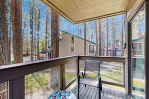 A covered deck with a mesh railing, a single chair, and a round table with a colorful geometric pattern. - Charming condo near the lake with pool, hot tub & washer & dryer (South Lake Tahoe)