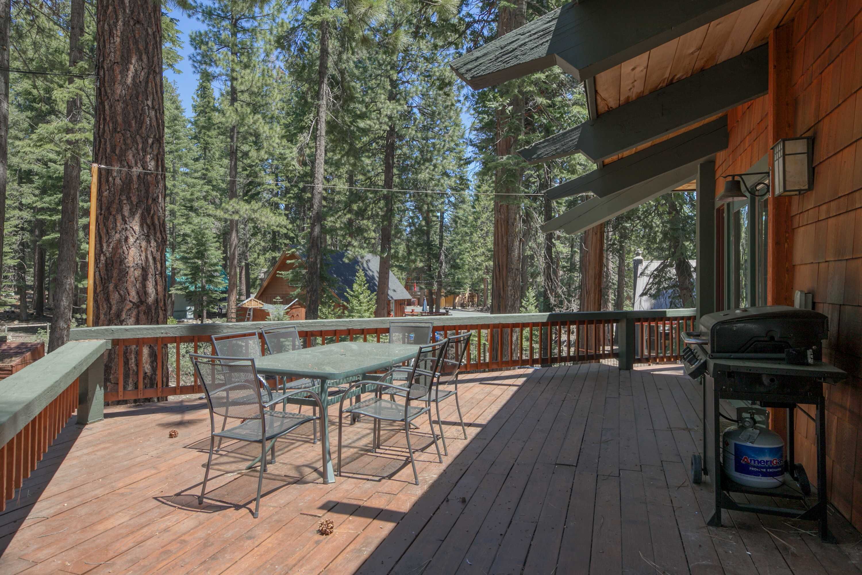 A wooden deck with a table and chairs, surrounded by tall trees.