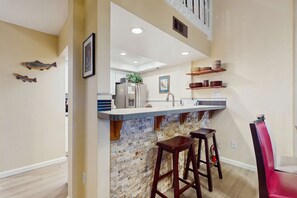 A kitchen with a stone backsplash, wooden bar stools, and a high ceiling with recessed lighting. - Updated Condo with Lake Views, Heated Floors, Soaking Tub (Stateline)