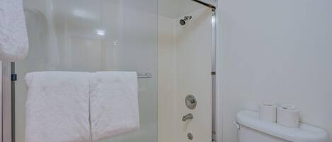 Un baño con ducha de vidrio, inodoro blanco y una toalla colgada en la pared.