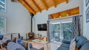 A modern living room with a fireplace, a flat-screen TV, and a large window with a balcony. - Charming Condo with Shared Hot Tub, Pool, Resort Amenities - Close to Ski & Beach (Carnelian Bay)