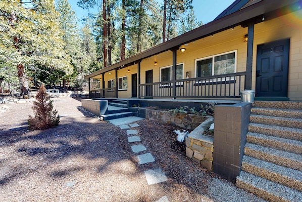 A lodge with a covered porch, stone steps, and a view of tall pine trees.
