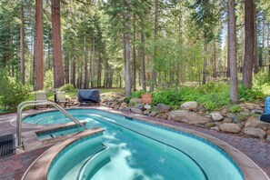 Une piscine dotée d’une terrasse en bois, entourée de grands arbres et d’un mur de pierre.