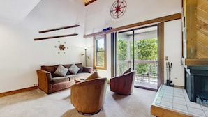 Een woonkamer met een bank, twee fauteuils, een open haard, een groot raam en een plafond met houten balken en een kompas decoratie.