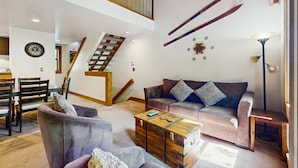 Een ruime woonkamer met een trap, een bank, een salontafel en een eethoek.
