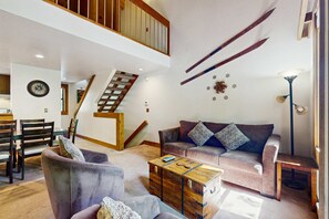 A spacious living area with a staircase, a sofa, a coffee table, and a dining area. - Mountain condo with access to outdoor pool, hot tub, tennis & sauna (NorthStar-Truckee)