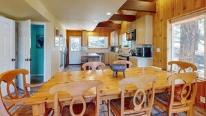 A wooden interior with a dining table and chairs, a kitchen area with appliances, and a view of trees. - Stateline Chalet -  5BR, Panoramic Mountain Views, Dipping Pool & Dry Sauna (Stateline)