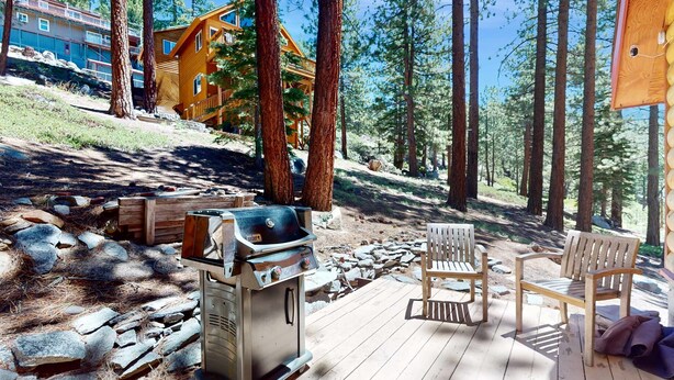 A wooden deck with a grill, two wooden chairs, and a view of a cabin in a forest. - Stateline Chalet -  5BR, Panoramic Mountain Views, Dipping Pool & Dry Sauna (Stateline)
