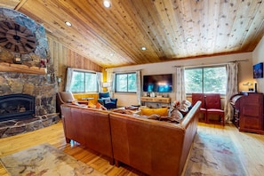 A cozy living room with a stone fireplace, leather sofa, wooden ceiling, and a flat-screen TV. - Cozy, dog-friendly, Tahoe home near rec centers for pools, gyms, & sports courts (Truckee)