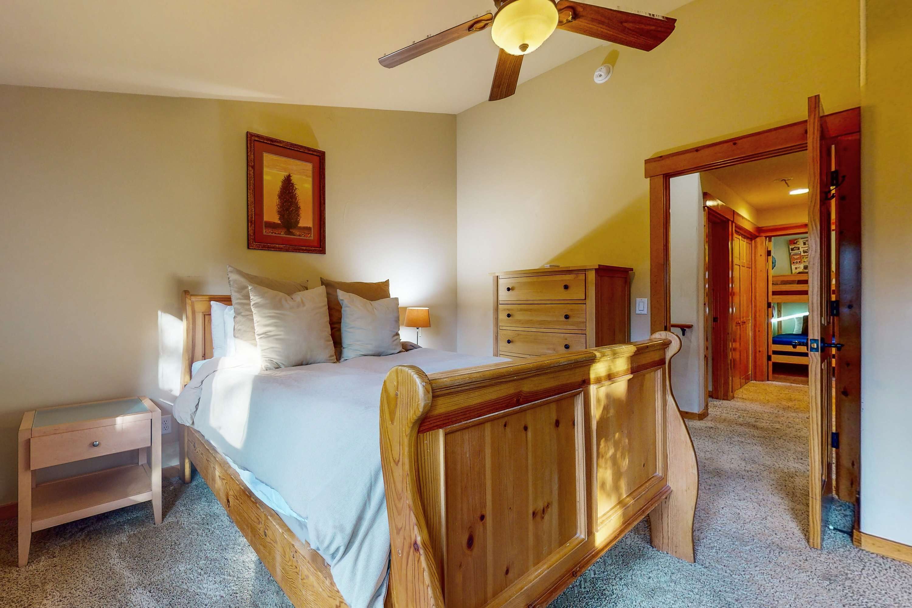 Een slaapkamer met een houten bed, nachtkastje, dressoir en plafondventilator.