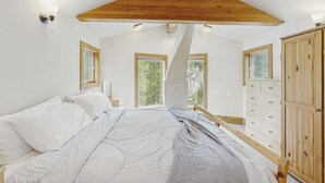 Ein Schlafzimmer mit einem Bett, einem Holzkopfteil, Fenstern und einer Kommode.