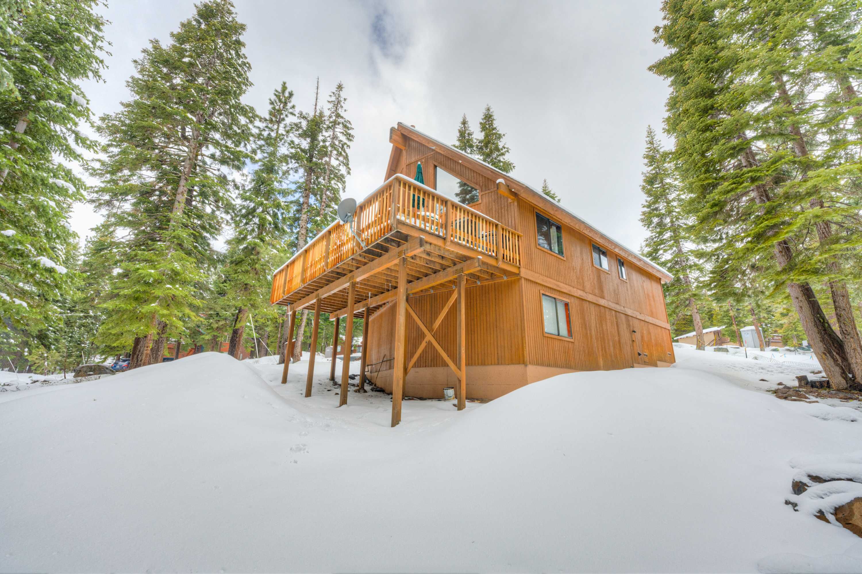 Une cabane en bois dotée d’un balcon, entourée de neige et de grands arbres.